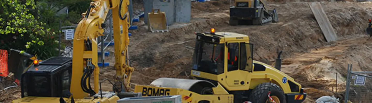 Different types of construction equipment in use at a site, supporting tasks like excavation, lifting, and barrier installation.