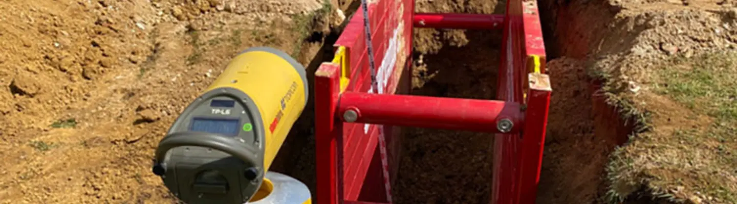 Pipe laser operating in trench with protective blue shield for pipe alignment             