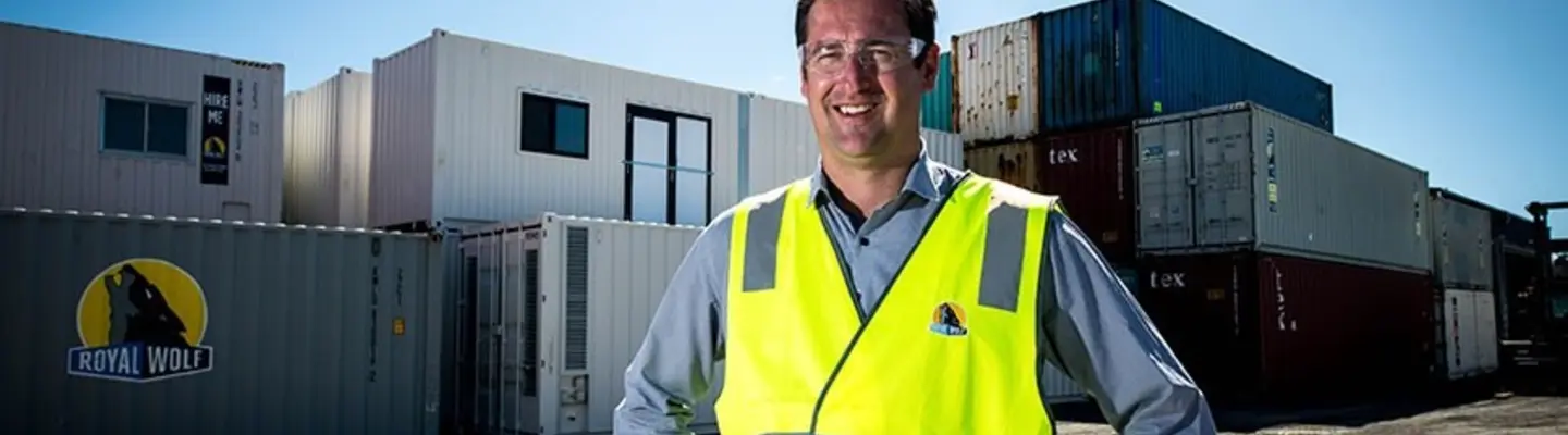 Manager standing in front of a stack of shipping containers at a work site, overseeing logistics and construction safety operations.