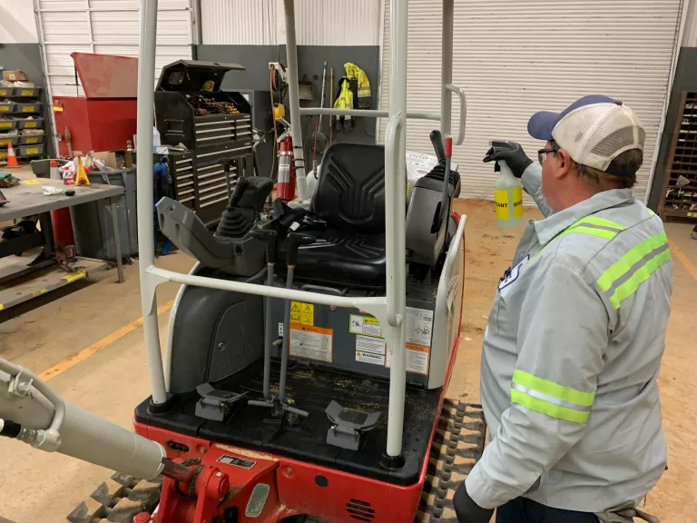 man cleaning backhoe for covid 19 response
