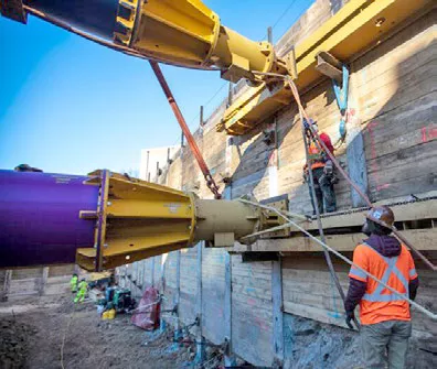 Interior of excavated trench as worker wearing a bright vest looks at hydraulic struts