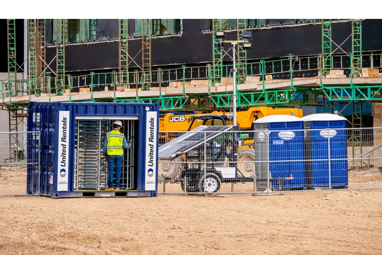 A worker using a turnstile to enter a jobsite on the left and porta potties on the right.