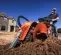 Orange Ditch Witch 36 in. 11-15 HP walk behind trencher being used by worker to dig dirt outside of a home