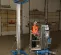 Elevador de materiales manual de 16 – 18 ft Genie azul sosteniendo una luminaria en un almacén