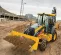 Yellow and black John Deere 4WD extended cab backhoe loader with a 19.5 ft. dig depth moving a load of dirt outside a construction site