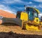 Yellow John Deere 100-115 HP low ground pressure bulldozer moving dirt next to a red brick building with a worker in the cab