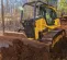 Yellow and black John Deere low ground pressure bulldozer moving dirt through a wooded area with a worker in the cab