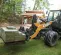 Orange and black Case wheel loader lifting a pallet of cement blocks in a wooded area with a worker in the cab and a worker in the background near a gazebo