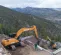 Orange Case excavator with boom extended and digging near a smaller Case excavator on the side of a mountain with workers present