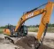 Orange and black Case excavator using its boom to dig dirt in a field with a worker in the cab