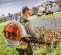 Orange and white Stihl backpack blower worn by a person blowing leaves