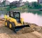 yellow skid steer on jobsite moving dirt in front of lake