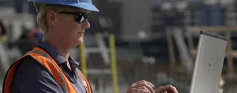 Worker at a jobsite wearing PPE and using a laptop computer
