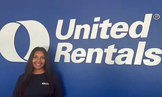 A woman standing in front of a blue wall with a big United Rentals logo on it.