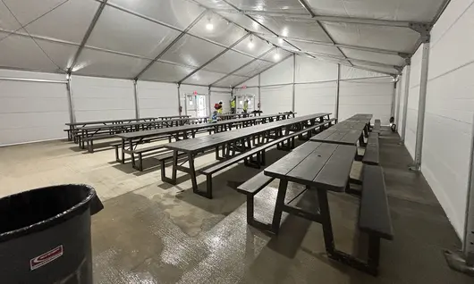 Rows of dark picnic tables arranged inside a spacious, brightly lit industrial tent, serving as a temporary breakroom.