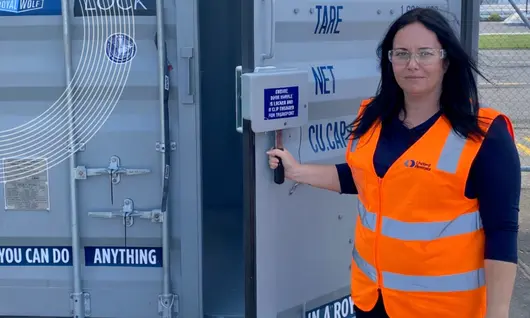 A woman in a hi-vis vest holding the door of a shipping container open.