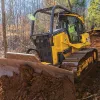 Yellow and black John Deere low ground pressure bulldozer moving dirt through a wooded area with a worker in the cab