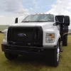 White Ford stake bed truck with a black lift gate parked facing forward in a grassy field