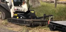 Slasher machine positioned in an open field, used for cutting grass or clearing vegetation near a worksite.