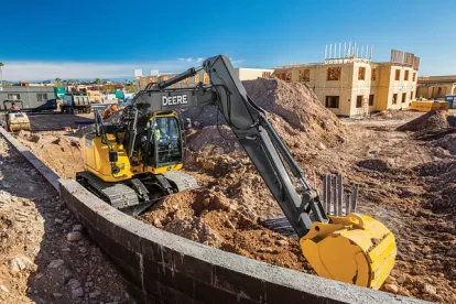 Yellow and black John Deere zero swing excavator digging dirt at a construction site