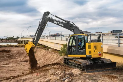 Yellow and black John Deere zero swing excavator dumping a load of dirt beside a freeway