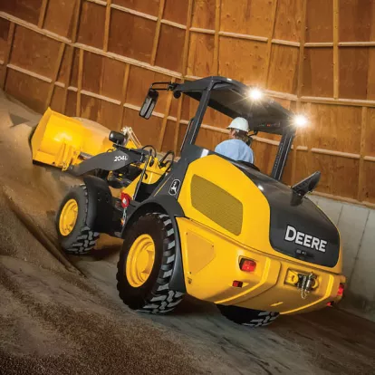 Yellow and black John Deere wheel loader moving dirt inside a building