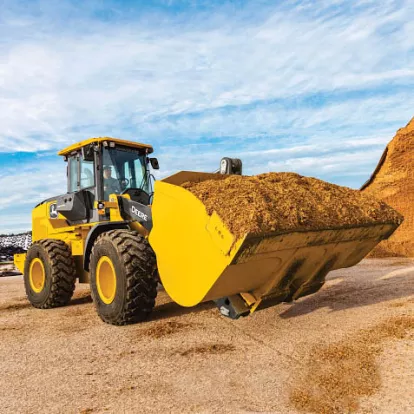 Yellow and black John Deere 4WD wheel loader carrying a load of dirt in its bucket