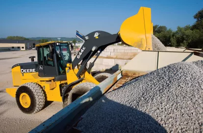 Yellow and black John Deere 4WD wheel loader dumping a load of material into a container