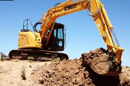 Yellow and black Kobelco zero swing excavator digging dirt at job site