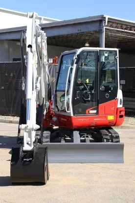 Red and white Takeuchi mini excavator parked in a warehouse lot