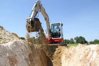 Red and white Takeuchi mini excavator lifting dirt from a deep hole