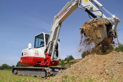 Red and white Takeuchi mini excavator lifting dirt from a pile