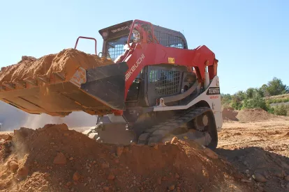 Red and white Takeuchi small track loader lifting dirt