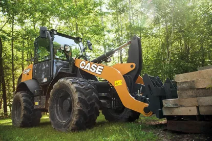 Orange and black Case wheel loader lifting a pallet of cement blocks in a wooded area