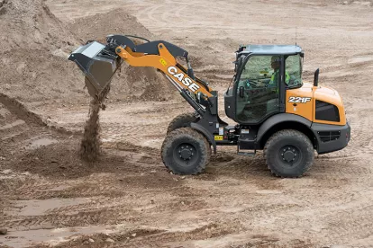 Orange and black Case wheel loader dumping dirt from its bucket with a worker in the cab