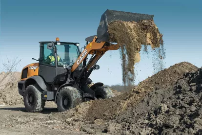 Orange and black Case wheel loader dumping a load of dirt from its bucket with a worker in the cab
