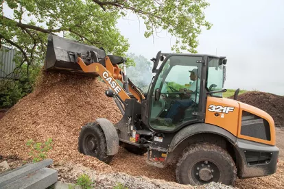 Orange and black Case wheel loader dumping a load of mulch from its raised bucket with a worker in the cab