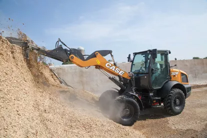 Orange and black Case wheel loader lifting mulch from a pile with a worker in the cab