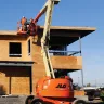 Photograph of a person using an orange articulating boom lift at a job site