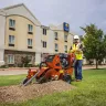 Orange Ditch Witch 48 in. walk-behind trencher in use next to a hotel parking lot