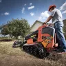 Orange Ditch Witch small skid steer loader being used for landscape work with a worker standing on the platform.