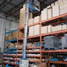Blue Genie 20 ft. electric powered fully extended vertical mast lift in a warehouse with a worker on the platform