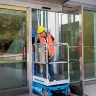 Blue Genie 21-25 ft. push around vertical mast lowered with worker moving through a glass exterior door