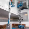 Blue Genie 30-33 ft. electric scissor lift with a worker on the platform next to a material lift inside a building