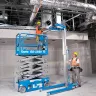Blue Genie electric powered scissor lift next to a material lift inside a building with workers
