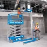 Blue Genie 30-33 ft. electric scissor lift with a worker on the platform next to a material lift in a warehouse