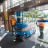 Blue Genie 20 ft. electric scissor lift going through double glass doors in a building
