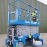Blue Genie 30-33 ft. electric scissor lift with battery pack exposed parked next to a metal building