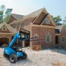 Blue Genie 6,000 lb. telehandler reach forklift with fork lifted parked in front of a home under construction