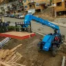 Blue Genie 8,000 lb. telehandler reach forklift with boom extended and carrying boards at construction site